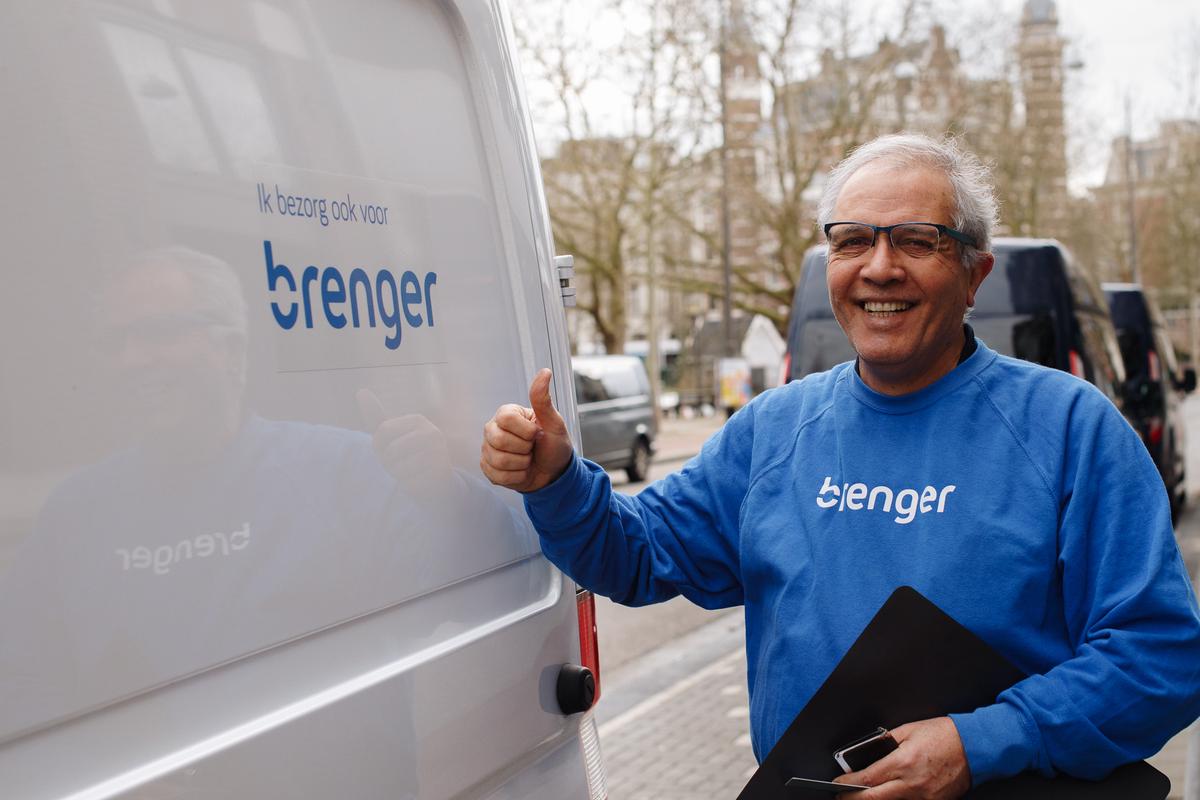 Brenger koerier met grijs haar en bril in een blauwe Brenger trui steekt duim omhoog naast witte bestelwagen met Brenger logo