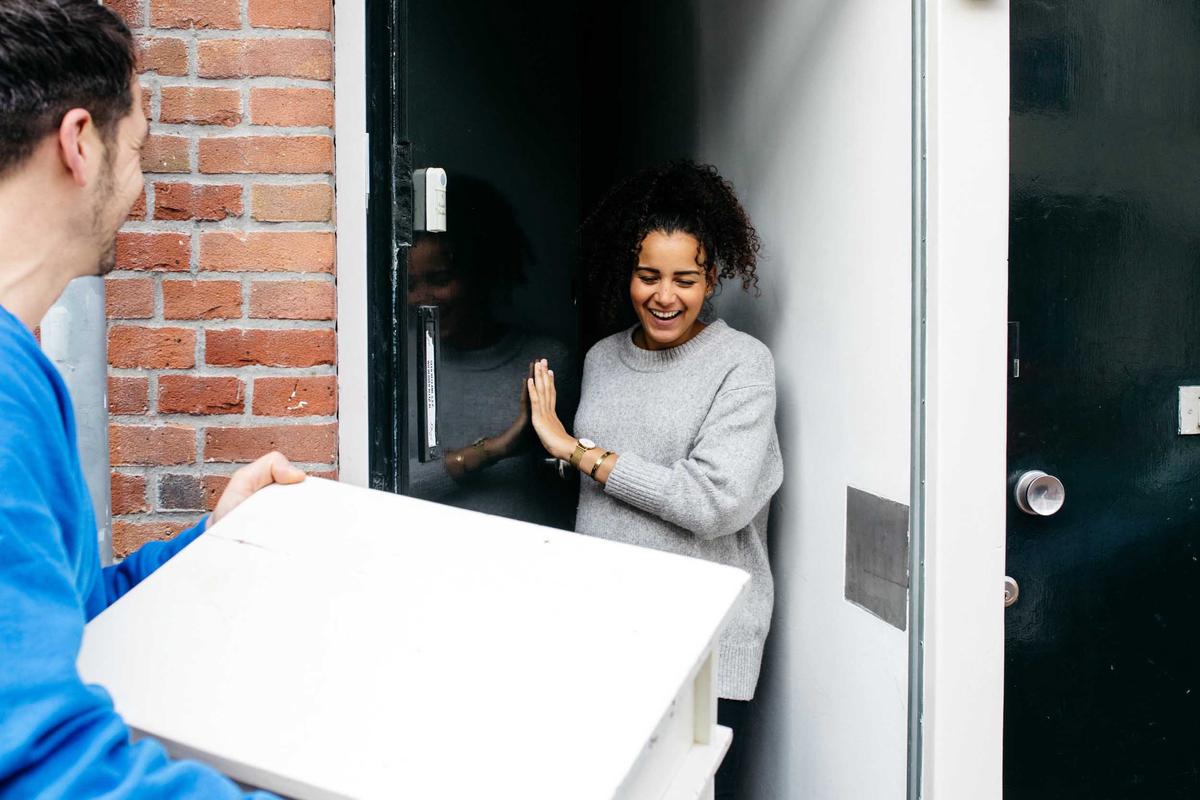 Bezorger overhandigt een witte meubel aan een lachende vrouw bij de deur