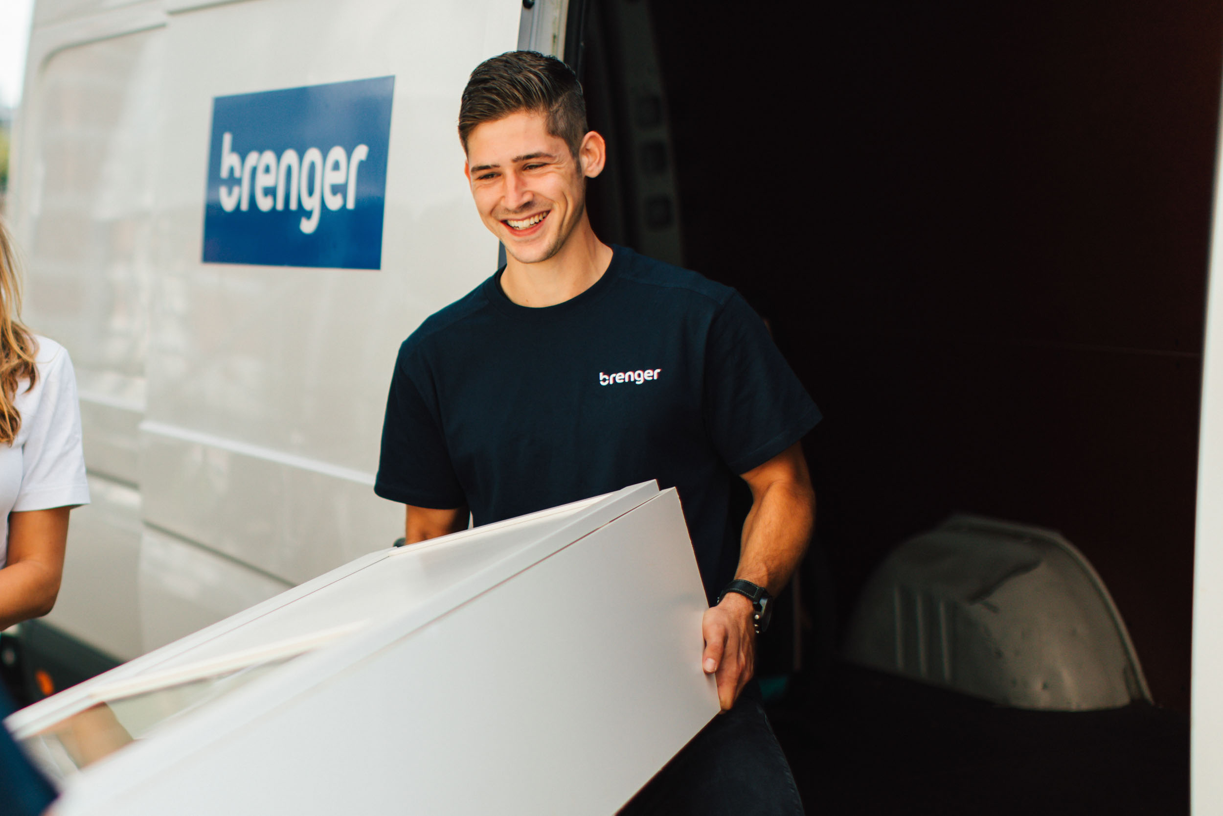 Man in donkerblauwe Brenger shirt tilt en witte meubel naast een witte Brenger bestelwagen