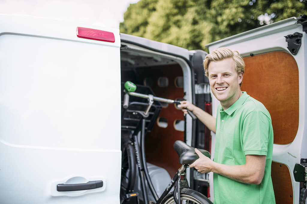 Glimlachende bezorger met groene polo plaatst een fiets in een bestelwagen.