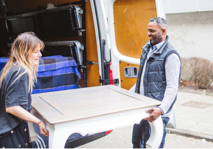 Een man en een vrouw tillen samen een tafel uit een bestelwagen tijdens een standaard stoeplevering van Brenger.